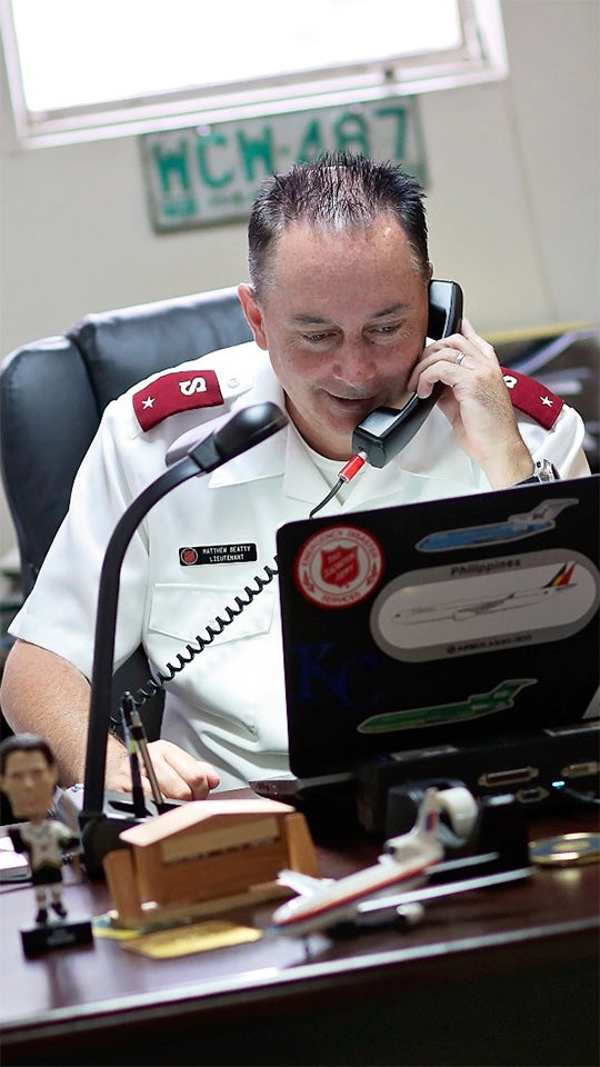 A Salvation Army officer sits at a desk, talking on the phone.