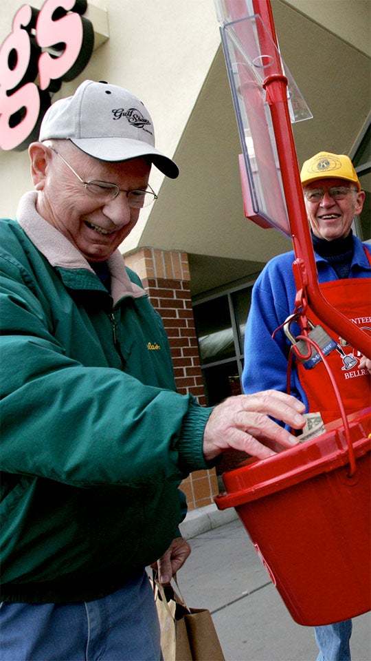 An older person donates to a Salvation Army Red Kettle outside of a supermarket.