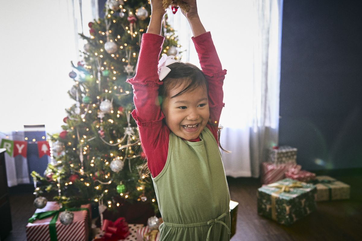 Girl celebrating with arms raised by a Christmas tree